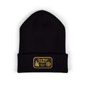 A black knit beanie hat with a folded cuff, featuring a rectangular yellow embroidered patch on the front that reads 'Clear Water Trading Co' with a tree and compass design, shown on a plain white background.