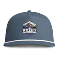 A slate blue snapback cap featuring a white stripe along the brim and a central embroidered patch with a mountain design and the text 'CLEAR WATER TRADING CO.'.