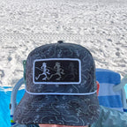 Person wearing a patterned cap with a logo, sitting on a beach chair.