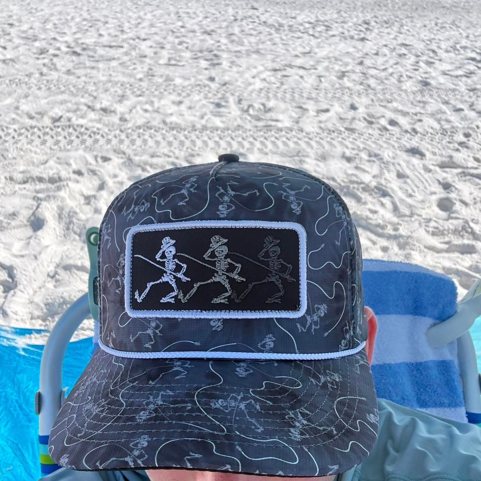 Person wearing a patterned cap with a logo, sitting on a beach chair.