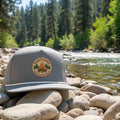 A slate blue snapback cap with a white stripe on the brim and a front patch reading 'RODEO' with a star and heart design, shown on a plain white background.
