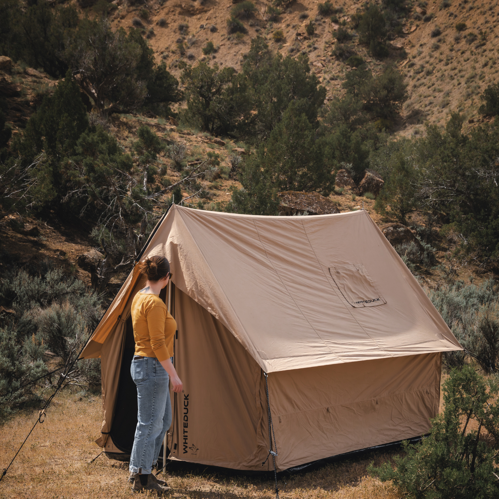 Person standing next to a beige tent in a natural outdoor setting