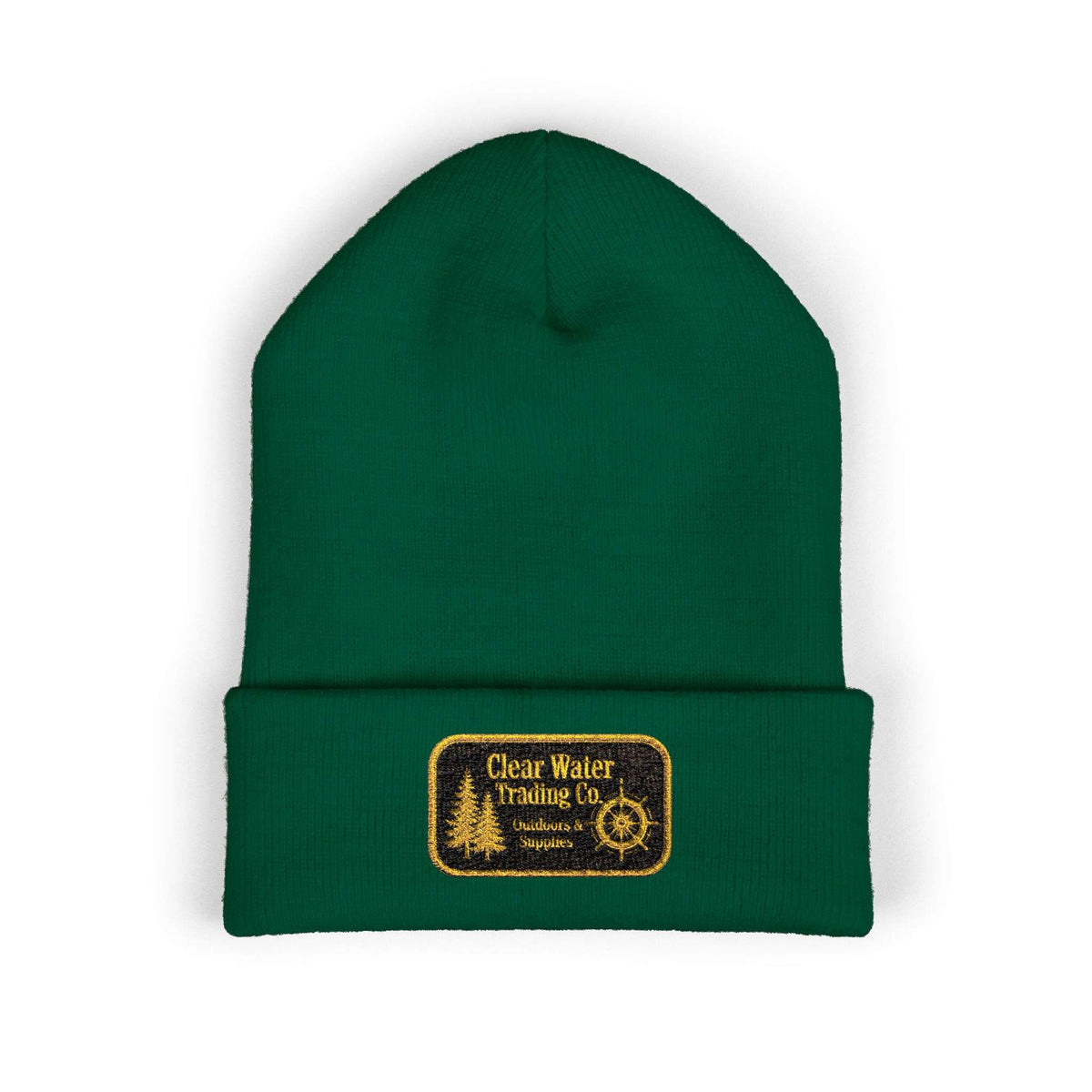 A dark green knit beanie hat with a folded cuff, featuring a rectangular embroidered patch on the front that reads 'Clear Water Trading Co' with a tree and compass design.
