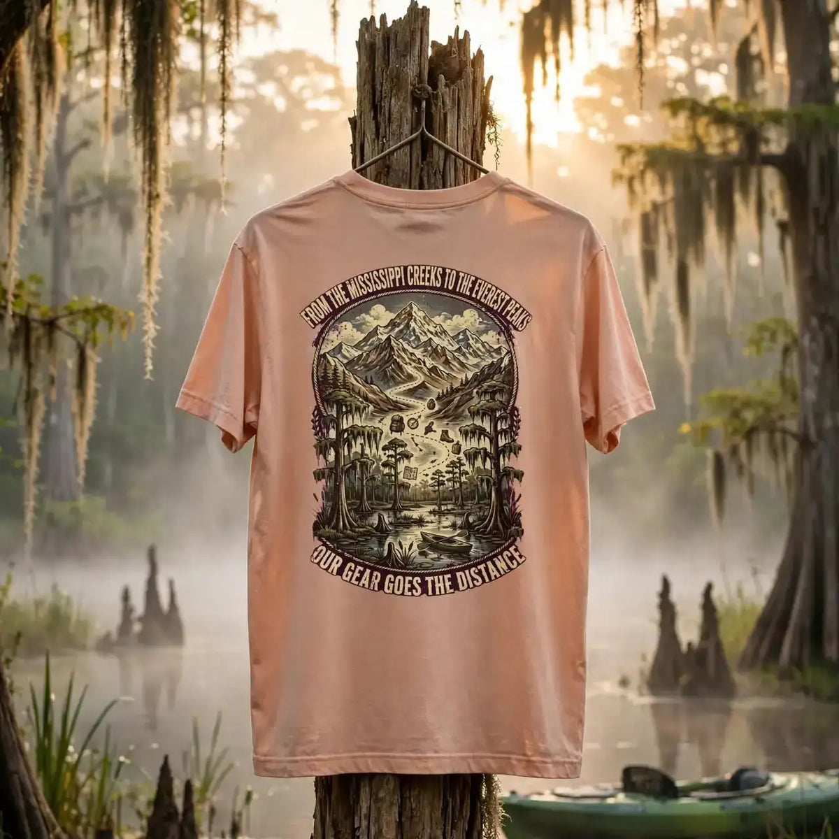 A peach-colored graphic t-shirt is displayed on a wooden post in a misty, mossy swamp setting at sunrise. The back of the shirt features a large black and brown graphic of a mountain landscape with the text 'ALL THE WOODS WHERE I HIDE ARE YOUR FOREST' and 'ALL BEAR WHO CATCH THE PREY'.