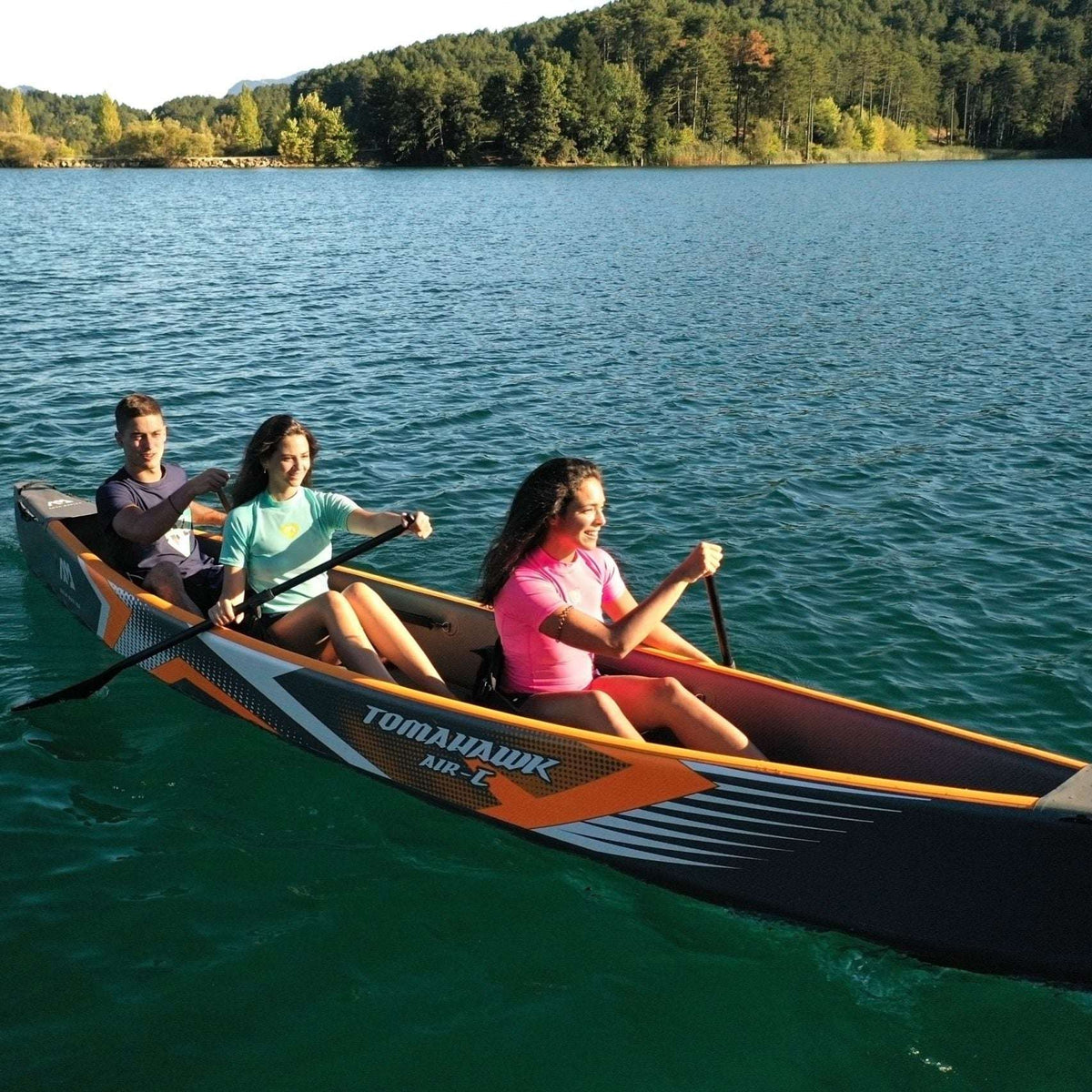 Three people in a canoe on a calm lake with trees in the background
