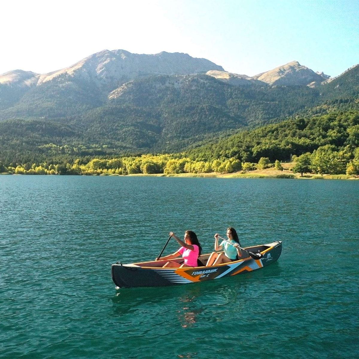 Two people in a kayak on a calm lake with mountains in the background