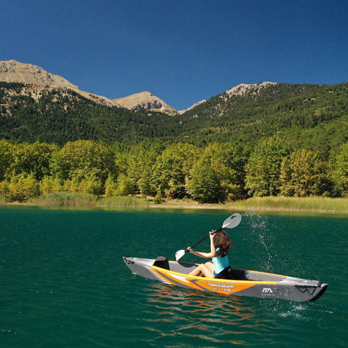 Person kayaking on a lake with mountains and trees in the background