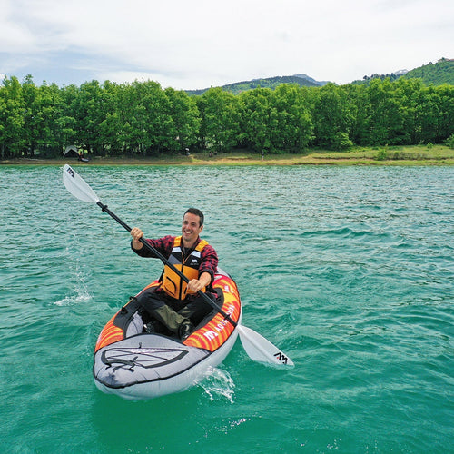 Person kayaking on a calm lake with trees and mountains in the background