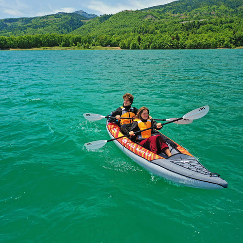 Two people in a kayak on a clear lake with mountains in the background