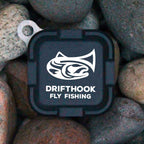 Drifthook Fly Fishing logo on a black square background surrounded by stones