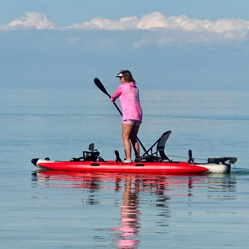 Person paddleboarding on a calm body of water with a clear sky.