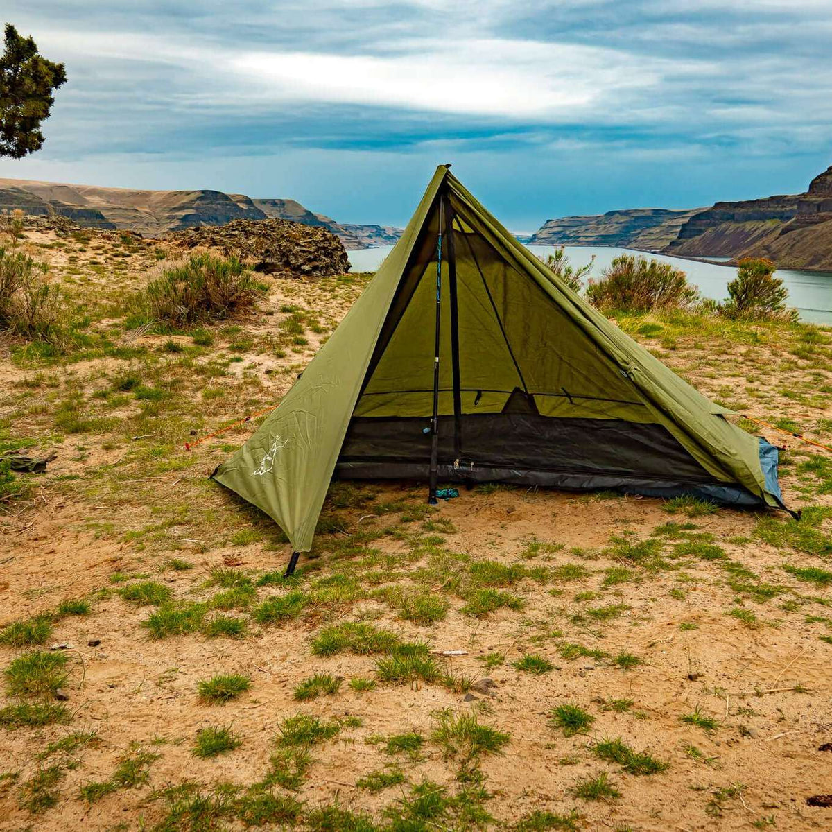Green tent set up in a desert landscape with mountains and a lake in the background.