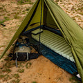 Green camping tent with a sleeping pad and backpack on a sandy ground